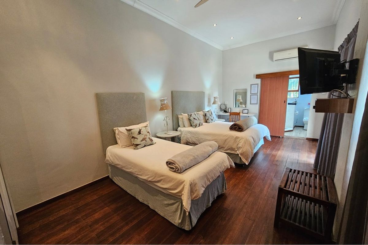 A well-maintained bedroom featuring rich hardwood flooring, recessed ceiling lighting, a wall-mounted air conditioning unit, and an en-suite bathroom access via a sliding door.