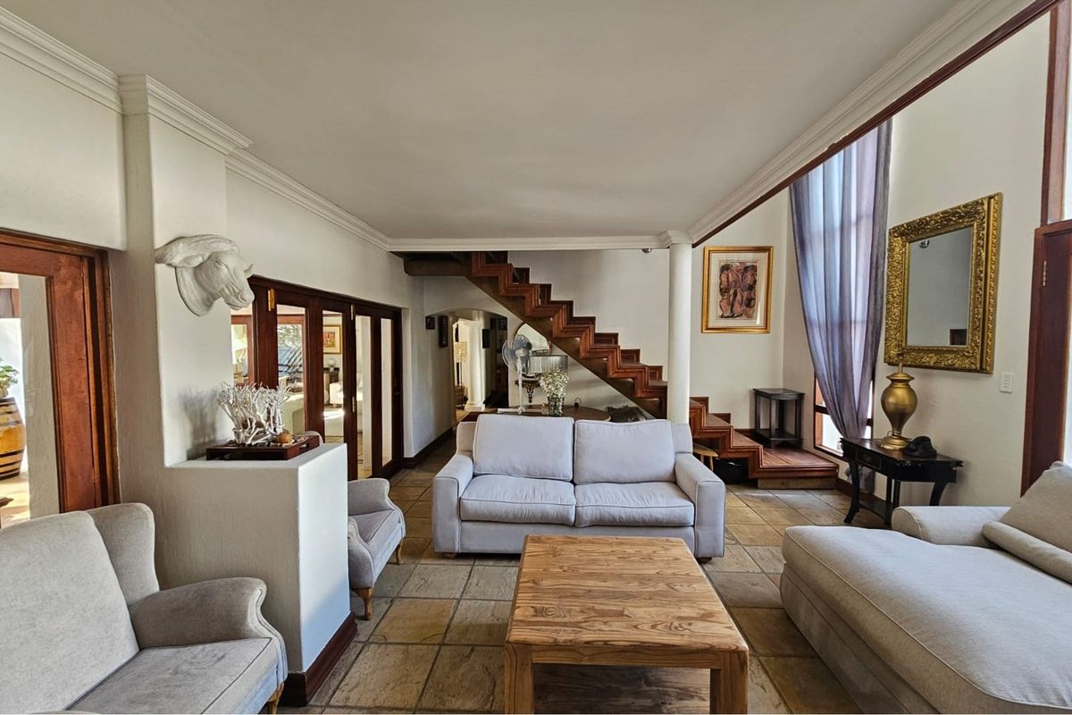 Spacious living area featuring natural stone flooring, a prominent wooden staircase, and large windows allowing for ample natural light.