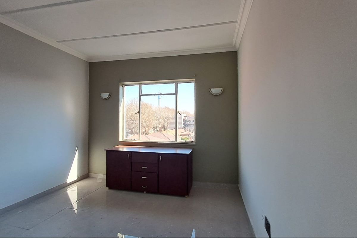 A bright, empty room featuring tiled flooring, neutral wall tones, and a large window providing natural light and an exterior view.