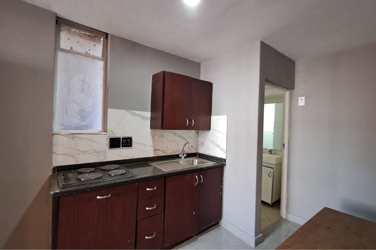 Compact kitchen area featuring dark wood cabinetry, a built-in electric hob, stainless steel sink, and marble-effect splashback tiling.