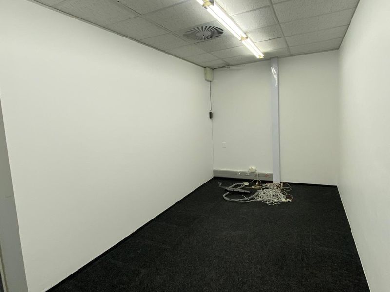 A vacant office space featuring a suspended acoustic ceiling, recessed lighting, air conditioning vent, and dark carpeting.