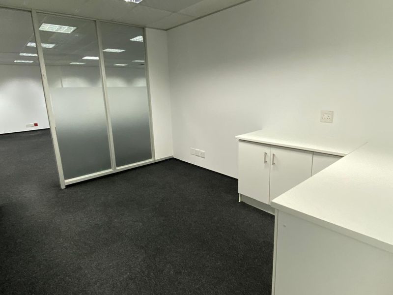 A clean, professional office space featuring built-in white cabinetry, dark carpeting, and a glass partition wall, providing a bright and functional work environment.