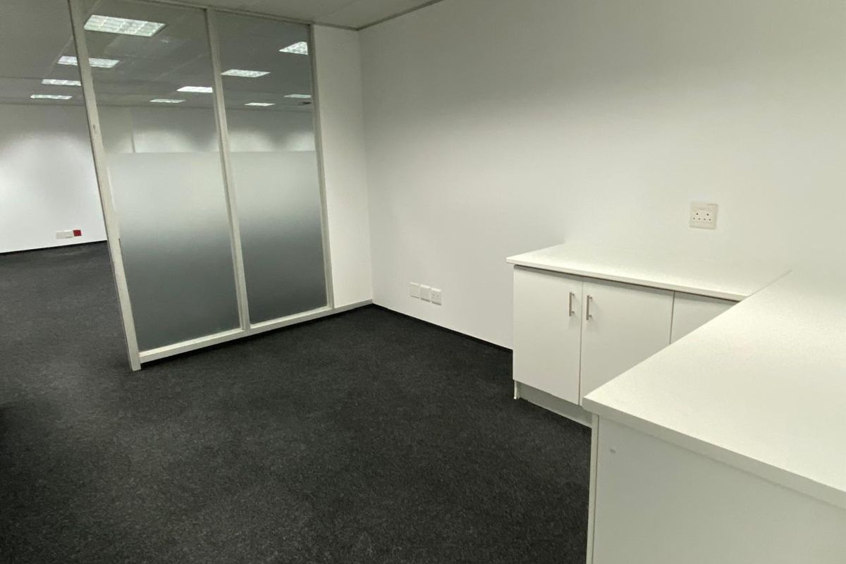 A clean, professional office space featuring built-in white cabinetry, dark carpeting, and a glass partition wall, providing a bright and functional work environment.