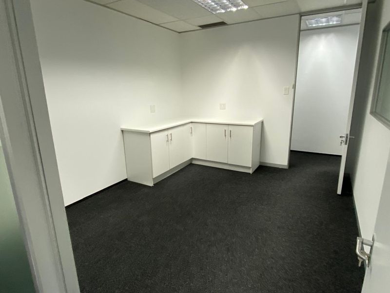 A clean, professional office space featuring built-in white cabinetry, dark carpeting, and a suspended ceiling with integrated lighting.