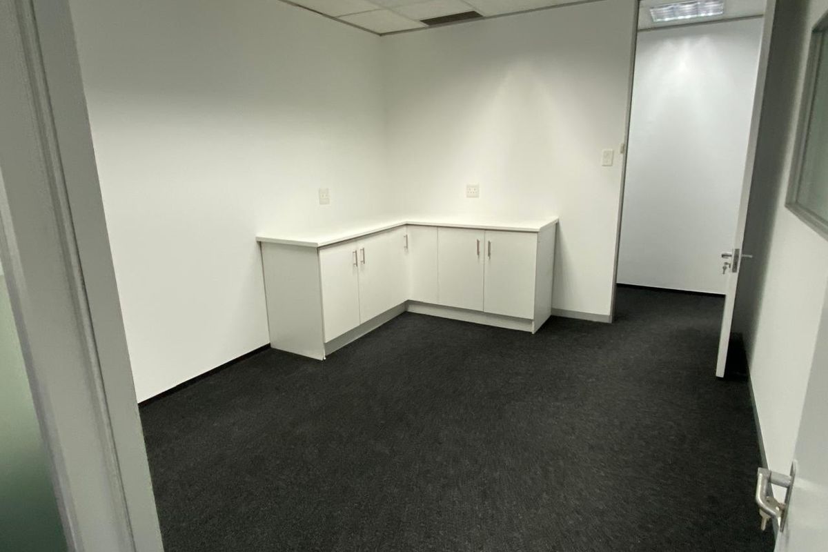 A clean, professional office space featuring built-in white cabinetry, dark carpeting, and a suspended ceiling with integrated lighting.