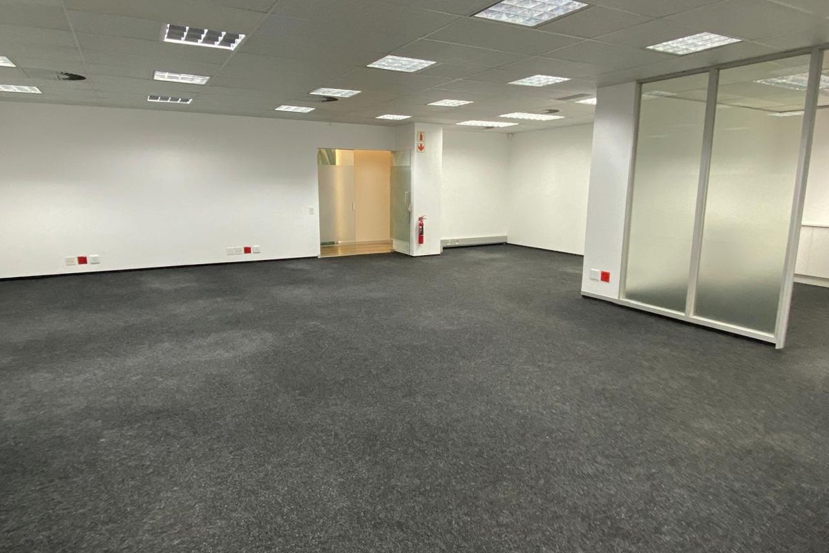 Spacious open-plan office area featuring a suspended ceiling with recessed lighting, glass partitioning, and wall-mounted electrical outlets.