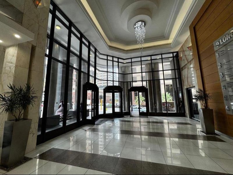 Spacious office building lobby featuring high ceilings, floor-to-ceiling glass facade, polished tile flooring, and a decorative crystal chandelier.