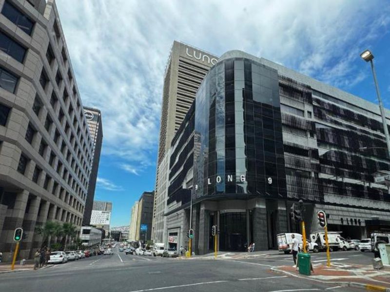 A street-level view of a modern commercial office building located on a corner, featuring glass facade elements and prominent signage.