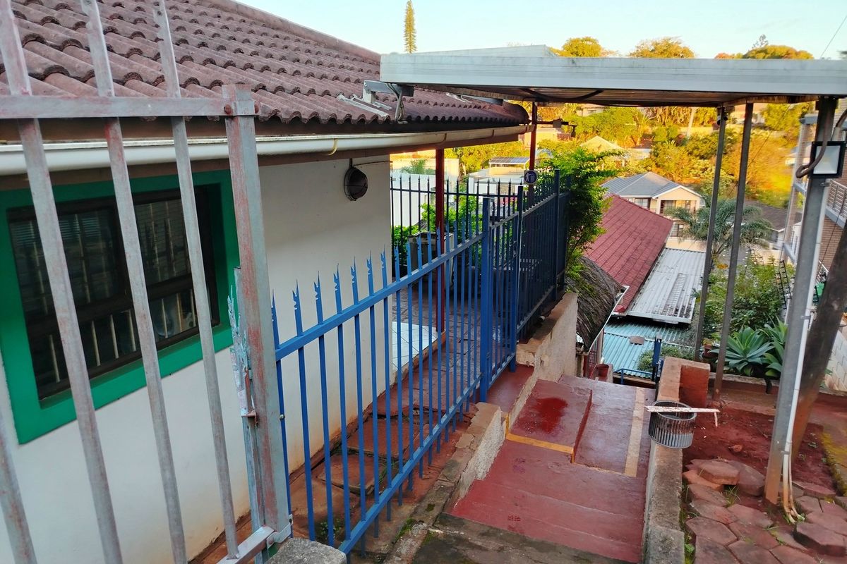 Exterior view of the property featuring a metal security fence, concrete staircase, and a covered outdoor area with tiled flooring.