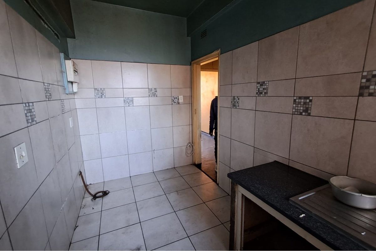 A dated kitchen area featuring tiled walls, a basic countertop, and plumbing connections, requiring renovation to modernize the space.