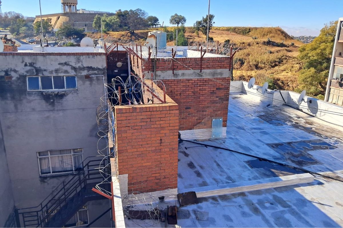 Elevated view of the building rooftop featuring exposed brick structures, security razor wire, and a weathered flat roof surface.