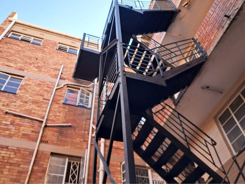 Exterior view of a multi-story brick building featuring an external metal fire escape staircase and steel-framed windows.