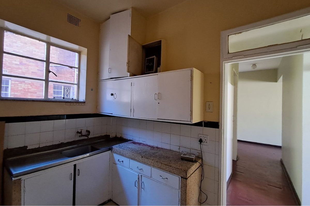 A dated kitchen featuring original built-in cabinetry, a stainless steel sink, and tiled backsplash, requiring renovation to modernize the space.