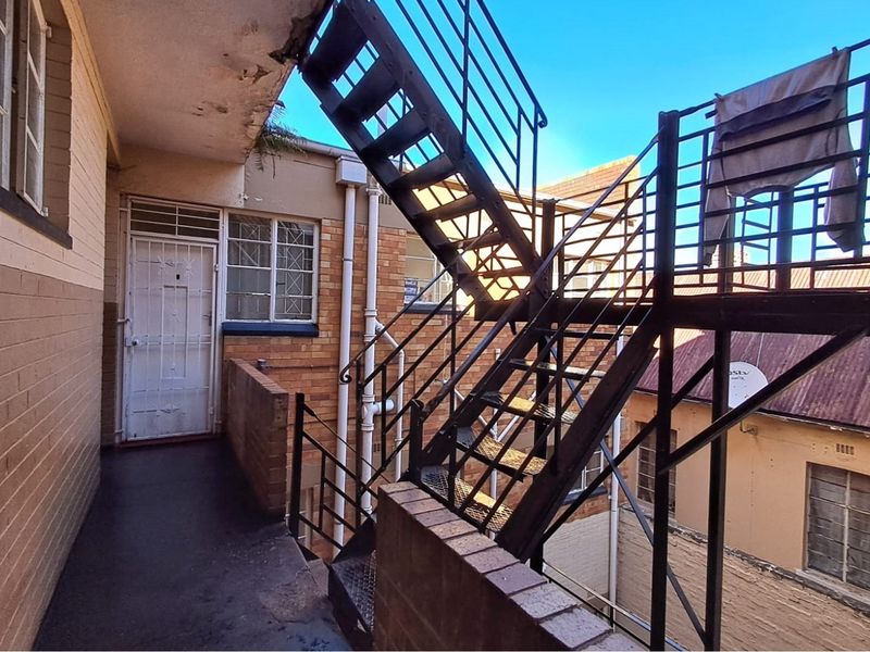 Exterior rear view of a retail property featuring a metal fire escape staircase, brick facade, and security access door.