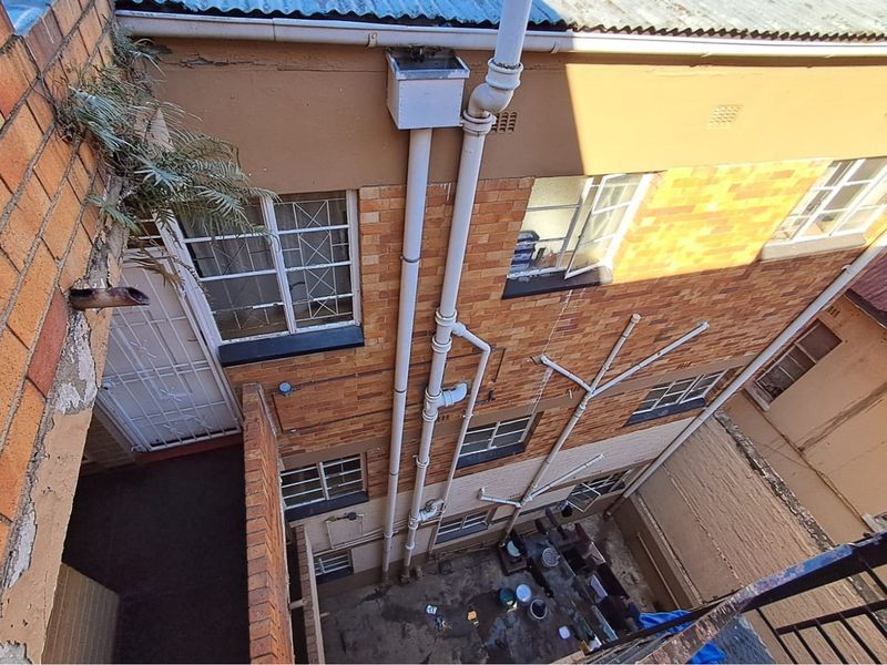 High-angle view of the rear building exterior showing brick facade, drainage infrastructure, and security window treatments.