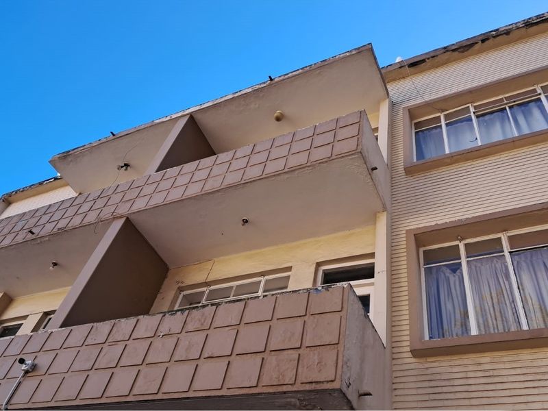 Low angle view of a multi-story retail or residential building facade featuring concrete balconies and tiled exterior finishes showing signs of wear.