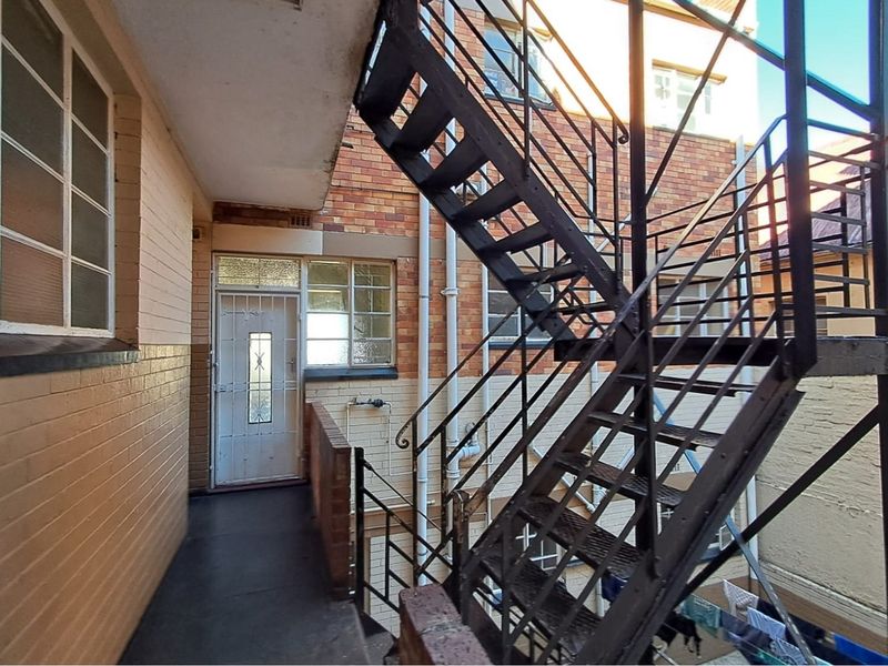 Exterior rear view of the property featuring a metal fire escape staircase, brick facade, and security entrance door.