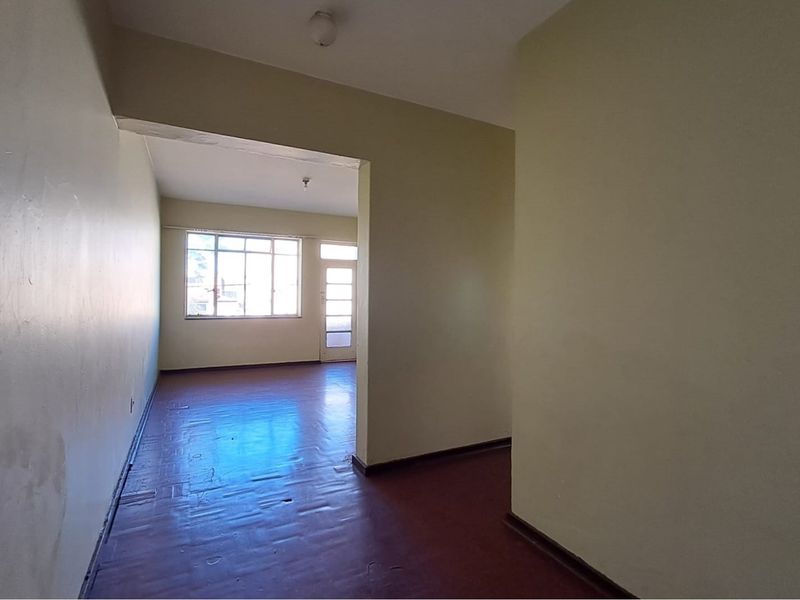 An empty, open-plan living area featuring original parquet flooring, large windows for natural light, and direct access to an exterior door.