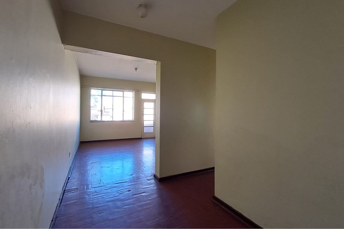 An empty, open-plan living area featuring original parquet flooring, large windows for natural light, and direct access to an exterior door.