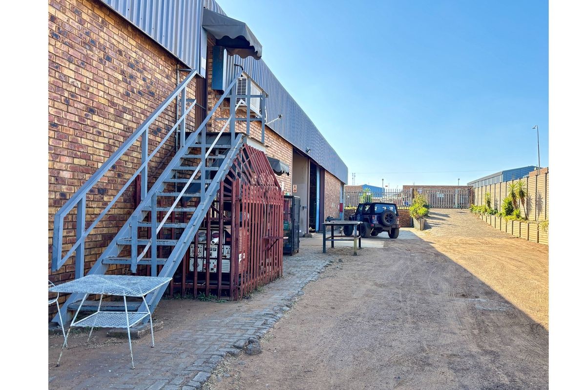 Exterior view of an industrial property featuring a brick facade, external metal staircase, and a gravel access area.