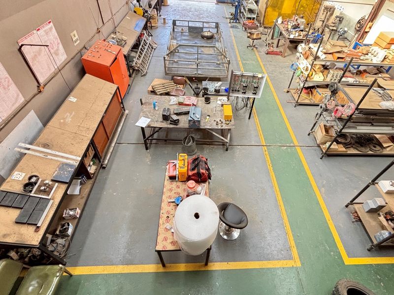 High-angle view of an industrial workshop space featuring concrete flooring with safety markings, built-in workbenches, and open storage shelving.