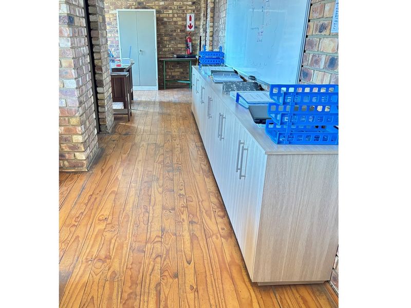 An industrial office space featuring exposed brick walls, timber flooring, and built-in cabinetry providing ample storage.