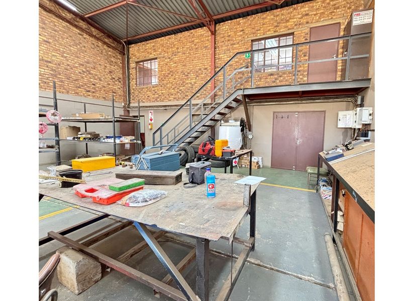 Industrial workshop space featuring exposed brick walls, high ceilings, a mezzanine level with metal staircase, and durable concrete flooring.