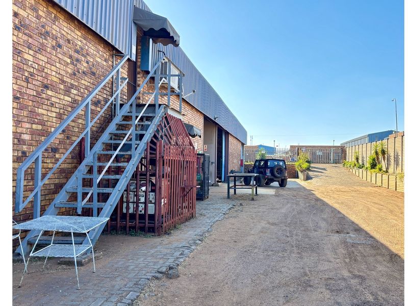 Exterior view of an industrial property featuring a brick facade, external metal staircase, and a gravel access area.