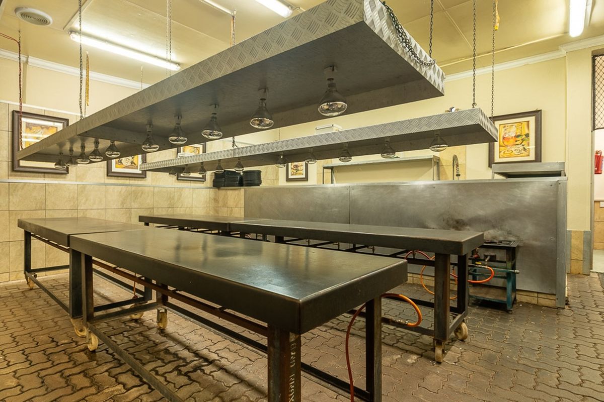 Commercial kitchen prep area featuring industrial stainless steel work tables, overhead heat lamps, and durable tiled flooring suitable for high-volume food preparation.
