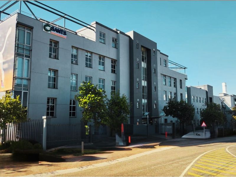 A multi-story office building facade featuring modern grey architectural finishes, large windows, and prominent signage, viewed from the adjacent street.