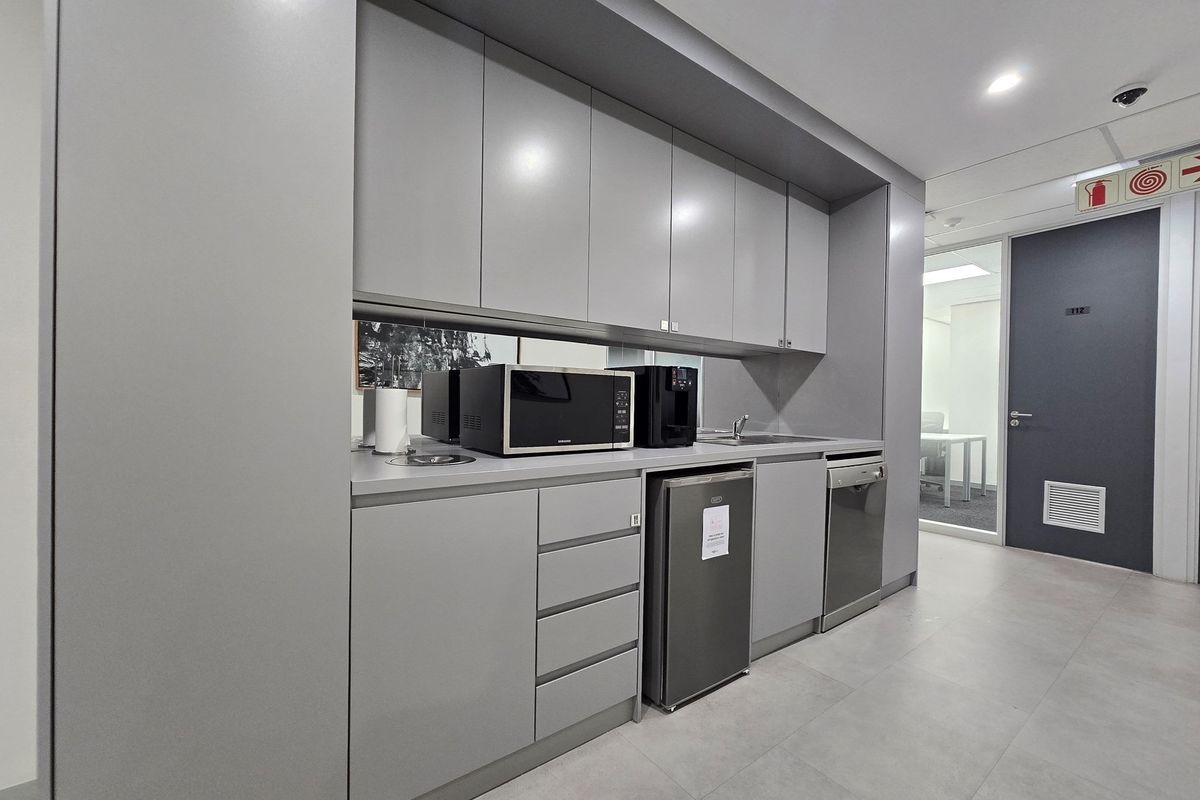 A modern office kitchenette featuring sleek grey cabinetry, a built-in sink, and integrated appliance space, providing a clean and functional break area.