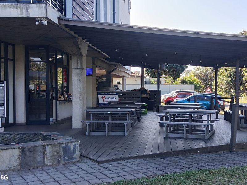 A covered outdoor patio area featuring a wooden deck, concrete structural pillars, and overhead lighting, providing an accessible exterior space for the office building.