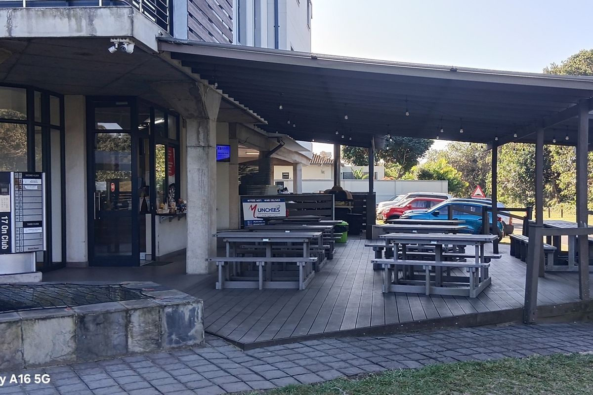 A covered outdoor patio area featuring a wooden deck, concrete structural pillars, and overhead lighting, providing an accessible exterior space for the office building.