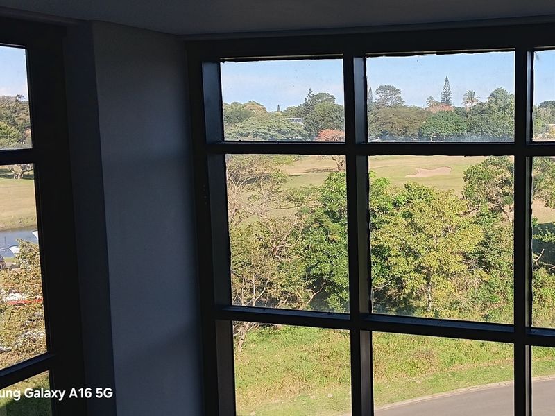 A view from an office space looking out over a green landscape and golf course through large black-framed grid windows.