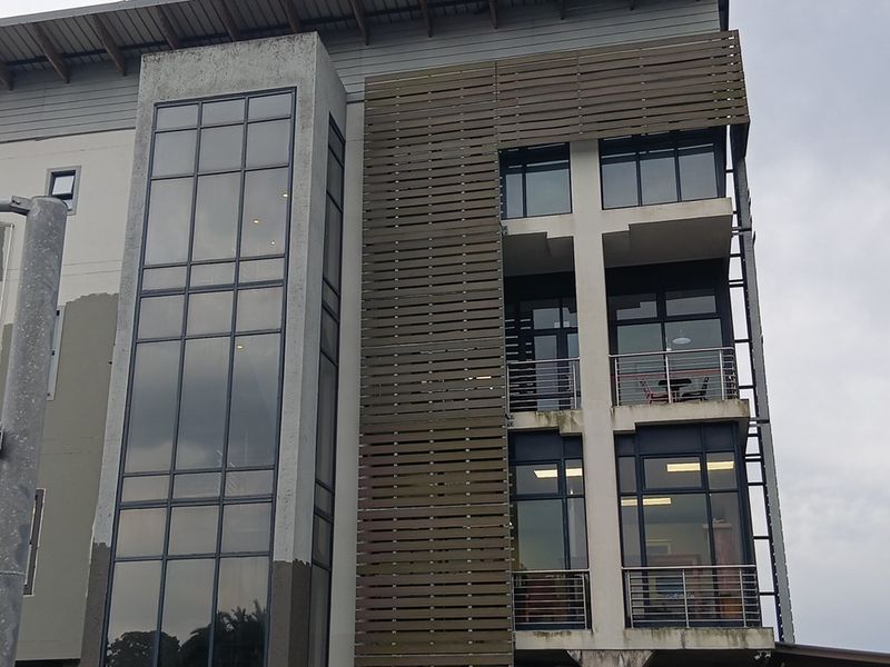 Modern multi-story office building facade featuring a combination of glass curtain walls, timber slat cladding, and private balconies with stainless steel railings.