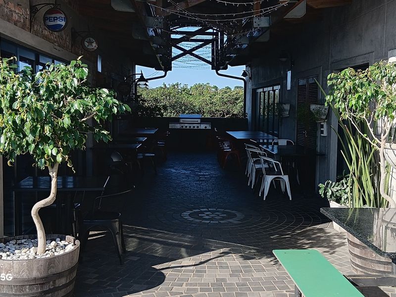 A covered outdoor patio area featuring exposed steel roof trusses, paved flooring, and a built-in braai station, suitable for office social gatherings.