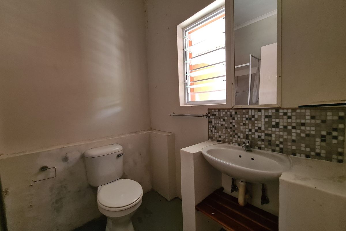 A functional bathroom featuring a pedestal-style basin with mosaic tile backsplash, a standard toilet, and a louvered window for ventilation.