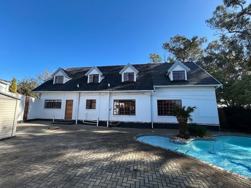 Rear exterior view of a commercial property featuring a tiled roof with dormer windows, a paved courtyard, and an adjacent swimming pool.