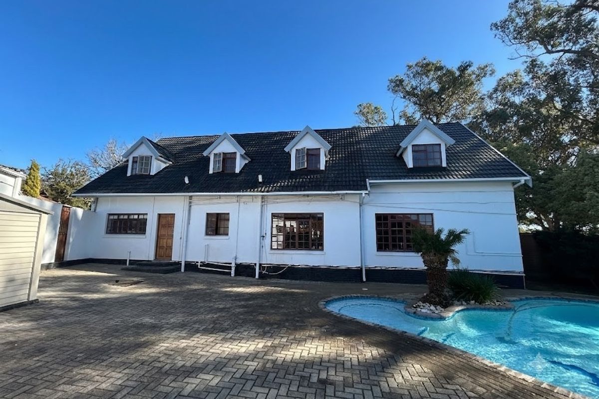 Rear exterior view of a commercial property featuring a tiled roof with dormer windows, a paved courtyard, and an adjacent swimming pool.