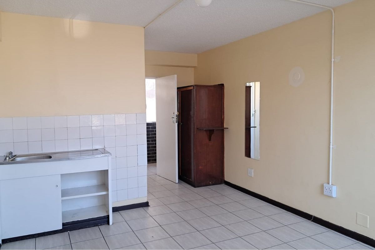 A basic kitchenette area featuring a simple sink unit with tiled splashback, ceramic floor tiles, and exposed electrical conduit.