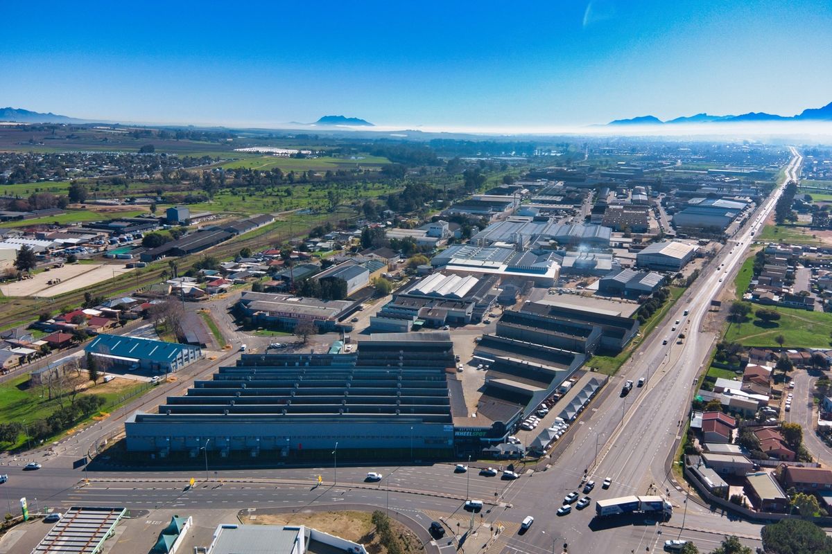 Aerial view of a large industrial retail park complex situated along a major road, featuring multiple warehouse structures and extensive parking facilities.