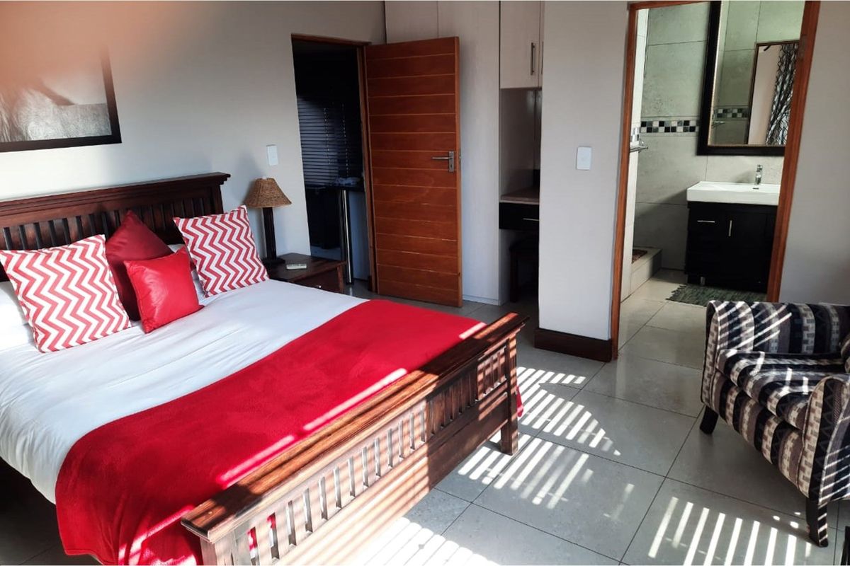 A well-maintained bedroom featuring tiled flooring, an en-suite bathroom with a vanity, and a wooden door leading to a secondary utility or storage space.