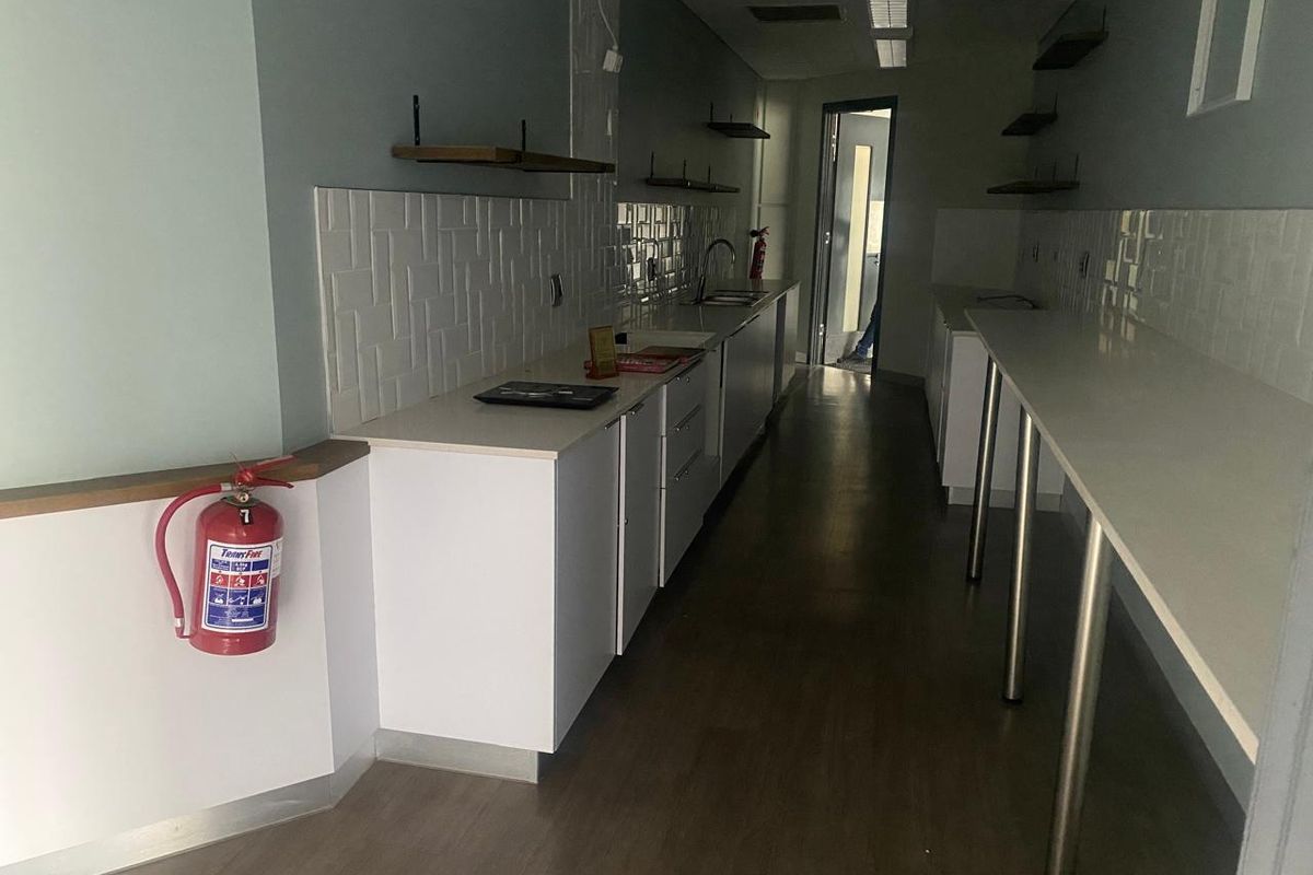 A clean, modern office kitchenette featuring white cabinetry, stone countertops, tiled backsplash, and integrated sink, providing a functional break area.