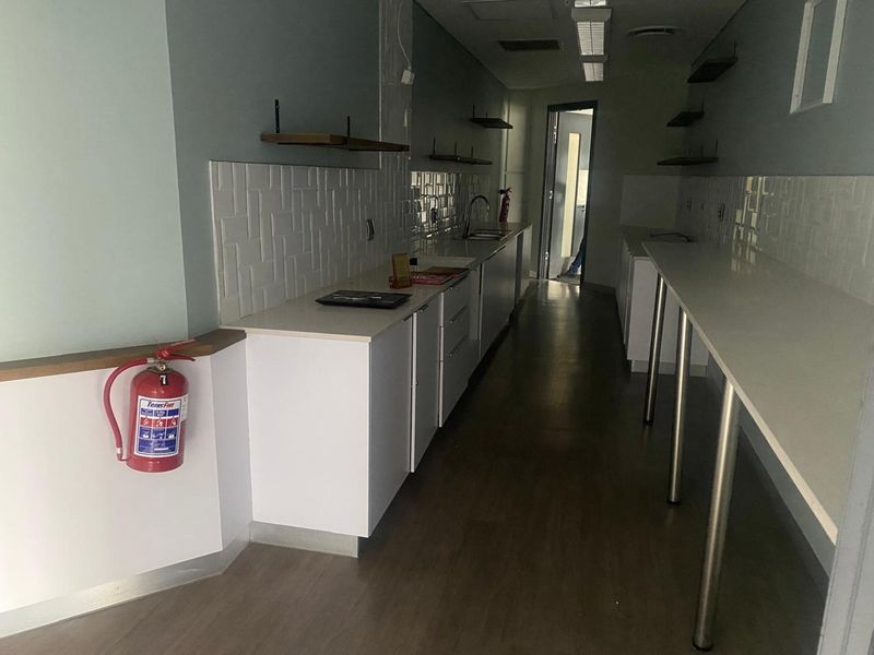 A clean, modern office kitchenette featuring white cabinetry, stone countertops, tiled backsplash, and integrated sink, providing a functional break area.