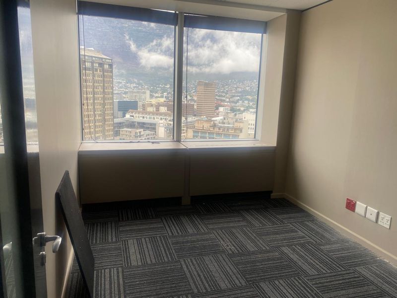 A vacant office space featuring carpet tiles, electrical and data connectivity, and large windows offering expansive city and mountain views.