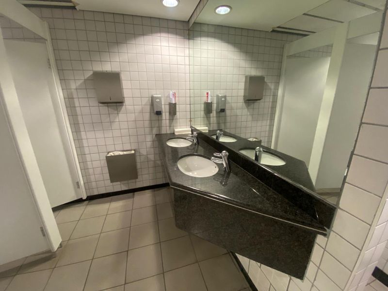 A functional office bathroom featuring a dual vanity with granite countertop, large wall mirror, and tiled surfaces throughout.