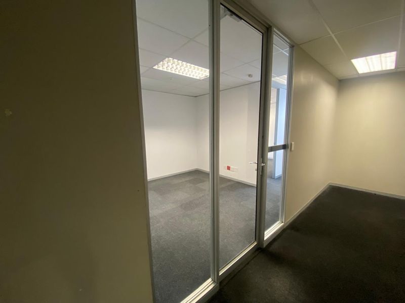 A vacant office space featuring a glass partition, carpeted flooring, and recessed ceiling lighting, providing a clean and professional environment.