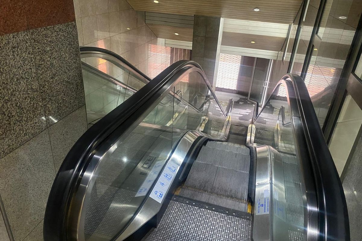A modern office building interior featuring a functional escalator with glass balustrades and polished granite wall finishes.