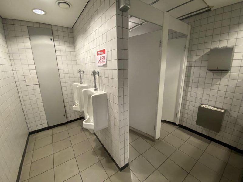 A functional commercial restroom featuring tiled walls and floors, multiple urinals, and partitioned stalls with integrated fixtures.