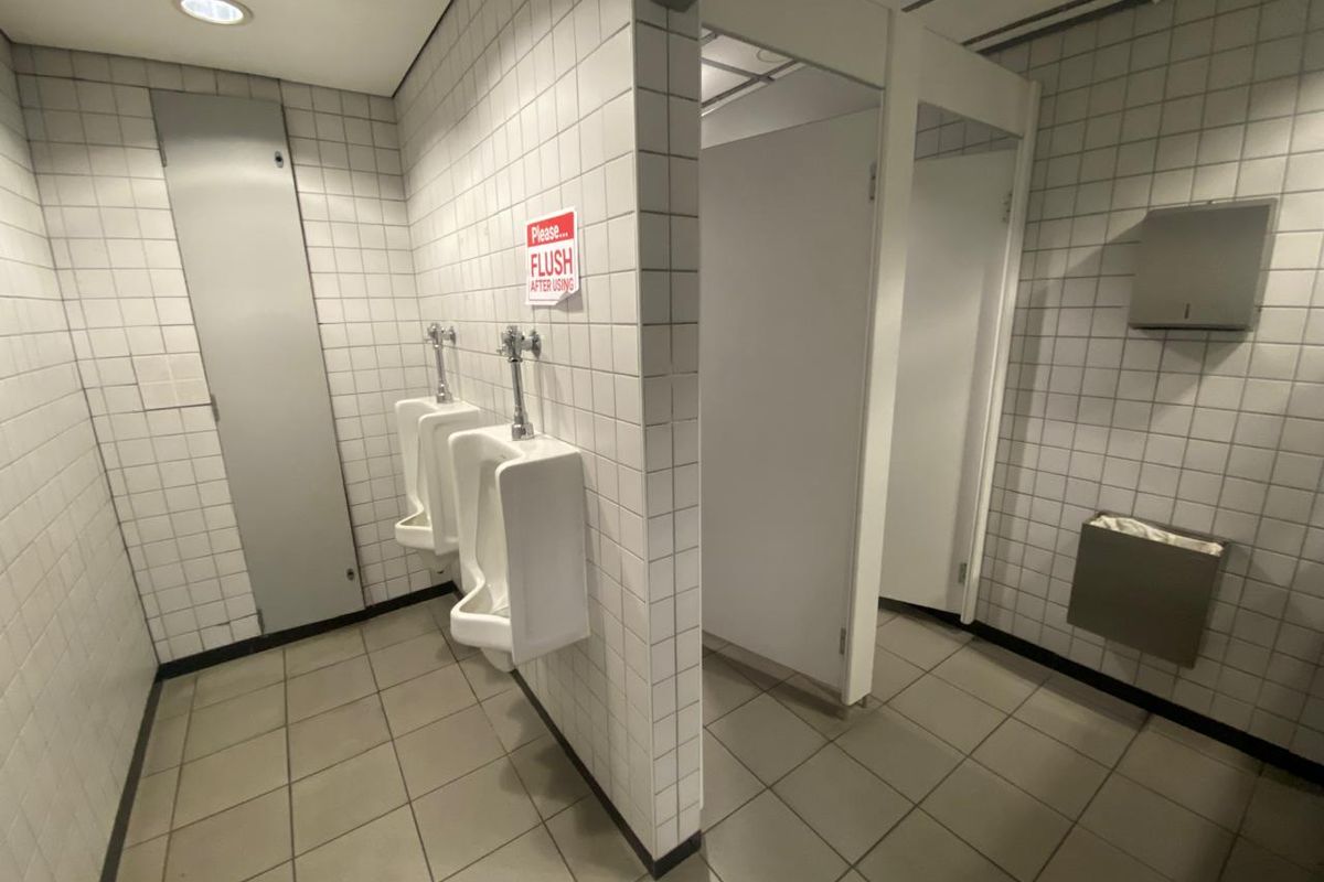 A functional commercial restroom featuring tiled walls and floors, multiple urinals, and partitioned stalls with integrated fixtures.